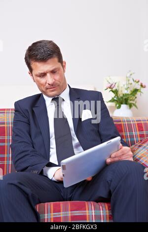 Manager in suit works on tablet computer on sofa Stock Photo