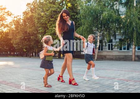 Mother's day. Happy woman meeting her kids daughters after classes outdoors primary school. Family goes home. Stock Photo