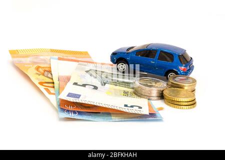 Stacks of giant silver coins and banknotes next to a blue used car Stock Photo