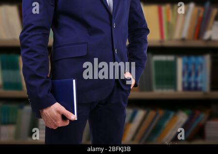 Male hand holding book on blurred bookshelves background Stock Photo
