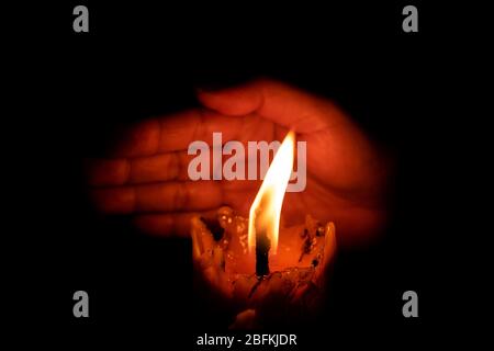 Hand protecting candle light from the wind in darkness on black background Stock Photo