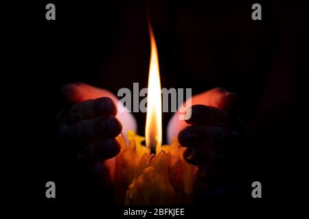 Close up hand protecting candle light from the wind in darkness on black background Stock Photo