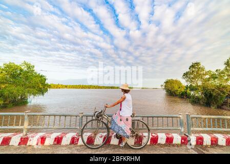 Tourist riding bicycle in the Mekong Delta region, Ben Tre, South Vietnam. Woman having fun cycling among green tropical woodland and water canals. Si Stock Photo