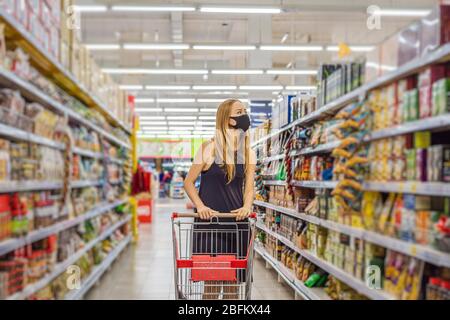 Alarmed female wears medical mask against coronavirus while grocery shopping in supermarket or store- health, safety and pandemic concept - young Stock Photo