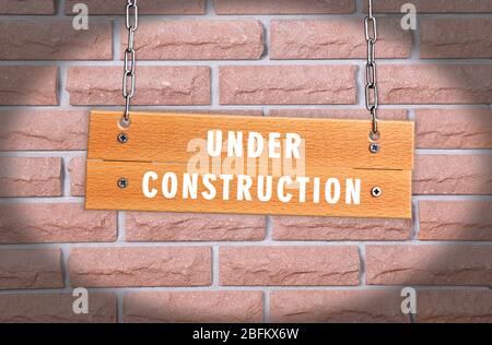 Wooden signboard with text Under Construction on brick wall background Stock Photo