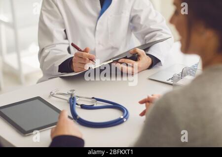 Confident doctor and couple patient sitting at the table in clinic office. Family doctor. Faceless. Stock Photo