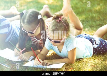 Happy active children lying on green grass and drawing in park Stock Photo