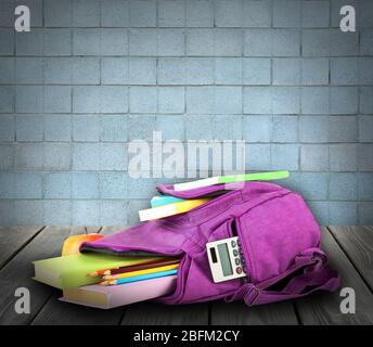 School backpack on wooden desk, on bricks wall background Stock Photo