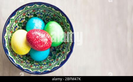 Colorful Easter eggs in bowl on white natural wooden background. Top view. Flat lay. Stock Photo