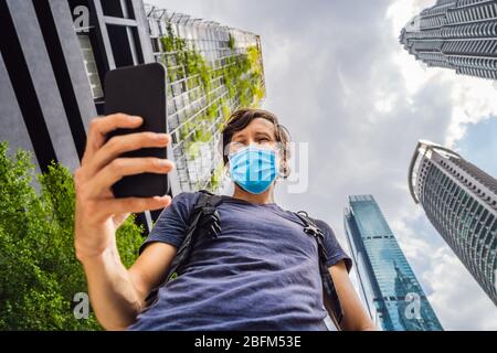 man in medical mask using map app on smartphone on the background of skyscrapers Tourists fear the 2019-ncov virus. Medical masked tourists Stock Photo