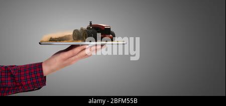 Farmer holding a tablet with autonomous tractor. Augmented reality and digital transformation in agriculture. Smart farming concept Stock Photo