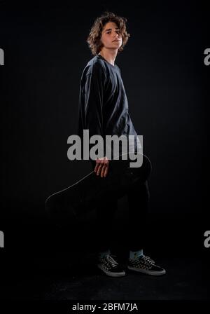 Studio body shot of a trendy young man wearing modern style clothes holding a skateboard Stock Photo