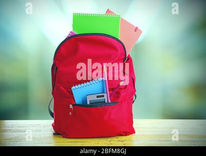 Red bag with school equipment on wooden table in classroom Stock Photo