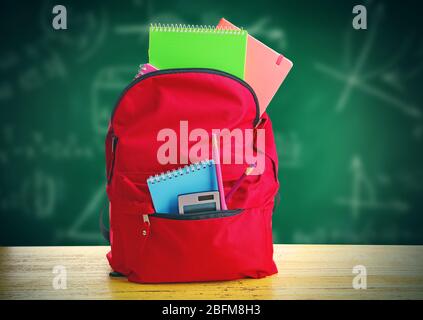 Red bag with school equipment on wooden table, near blackboard Stock Photo