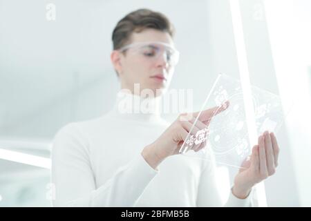 Hands of young contemporary app developer in white jumper and smart goggles pointing at display of transparent futuristic mobile gadget Stock Photo