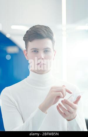 Young handsome software developer pointing at transparent mobile gadget while going to push button on display and looking at you Stock Photo