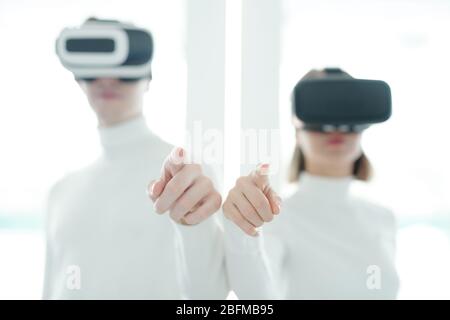 Hands of two young developers of futuristic apps or technologies in vr headsets pointing at virtual display while testing new software Stock Photo