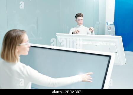 Two young progressive software developers looking through database on large interactive displays while working individually in office Stock Photo