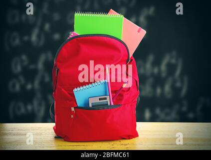 Red bag with school equipment on wooden table, near blackboard Stock Photo