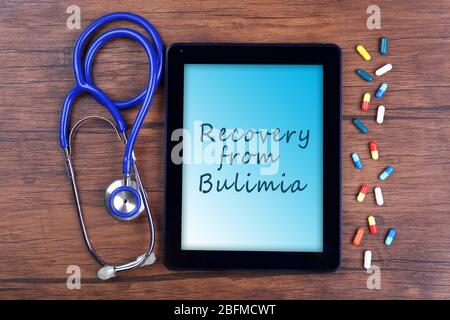 Tablet pc and text Recovery from Bulimia on screen on wooden background Stock Photo