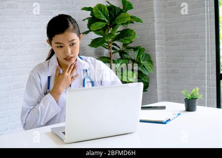 Online video conference chat with Asian female doctor and patient while discussing and diagnosing on laptop and looking at camera. Stock Photo