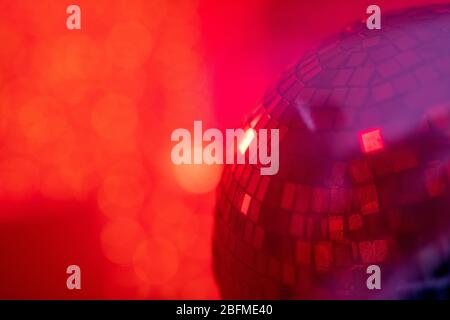 Part of large sparkling and rotating disco ball in night club against red smoky background with copyspace for your note or advertisement Stock Photo