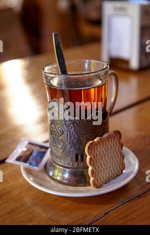 Glass of tea in an old vintage metal holder with cookie and sugar on a wooden table Stock Photo