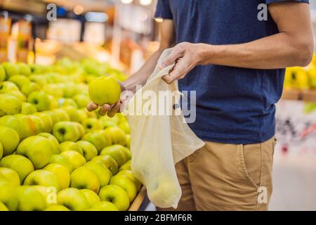 Man chooses apples in a supermarket without using a plastic bag. Reusable bag for buying vegetables. Zero waste concept Stock Photo