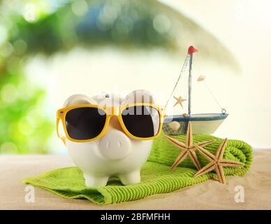 Piggy bank with towel and sunglasses on a sand. Holiday money concept Stock Photo