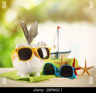 Piggy bank with dollar banknotes, towel and sunglasses on a sand. Holiday money concept Stock Photo