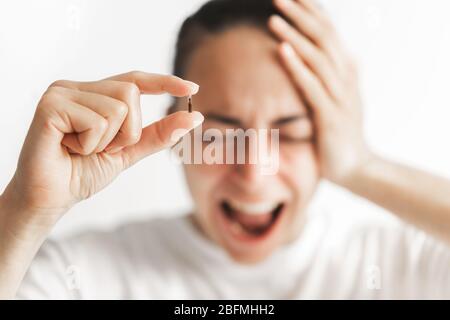 Person holding in fingers micro chip for implantation with defocused screaming face on background. Fear of government control. Future mandatory chipization of people. Stock Photo