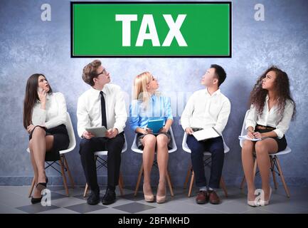 Tax concept. Young people sitting on a chairs in grey hall Stock Photo