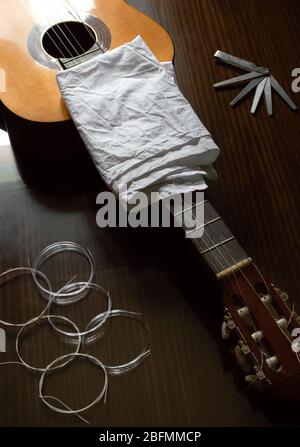 Top view of a guitar ready to change the strings. Classical guitar, set of new strings and tools on wooden table. Stock Photo