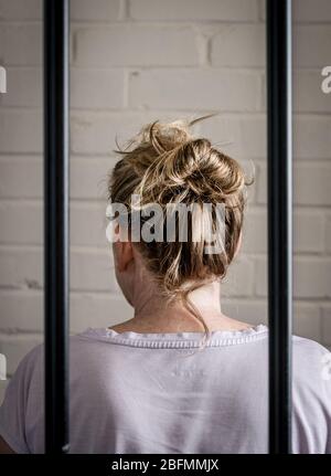 A Female prisoner behind bars in a woman prison. Picture posed by model.