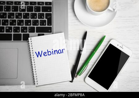 Webinar written in notebook, laptop, phone, pens and cup of coffee on table, top view Stock Photo