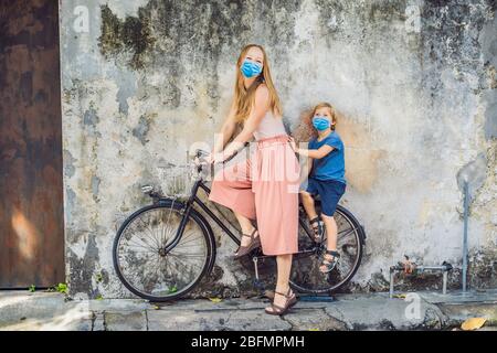 Mother and son in medical mask on a bicycle. Public street art Name Children on a bicycle painted 3D on the wall that's two little Chinese girls Stock Photo