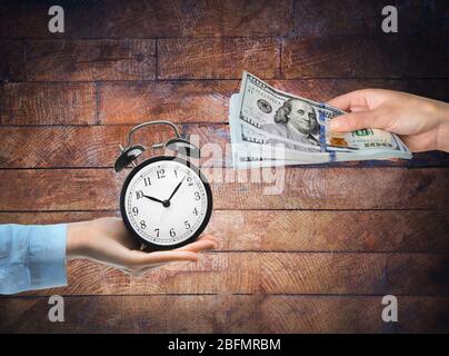 Time is money. Buying time. Hand with piggy bank and hand with alarm-clock, on wooden background Stock Photo