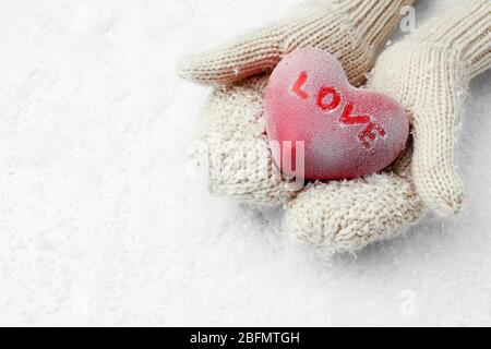 Female hands in mittens holding red heart on snowy background Stock Photo