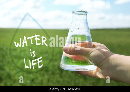 Female hand with flask and Water is Life text in drop frame on natural background Stock Photo