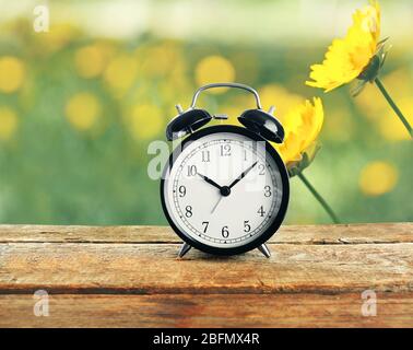 Summer time concept. Alarm clock on wooden table, cosmos flowers in the field background Stock Photo