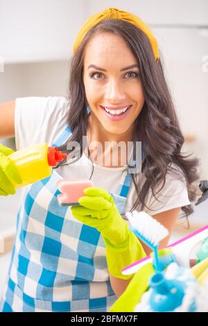 Smiling housekeeper looking into the camera pouring detergent onto a sponge. Stock Photo