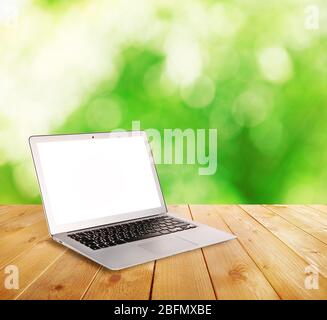 Laptop over wooden table on natural  green blurred background Stock Photo