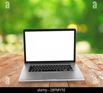 Laptop over wooden table on natural  green blurred background Stock Photo