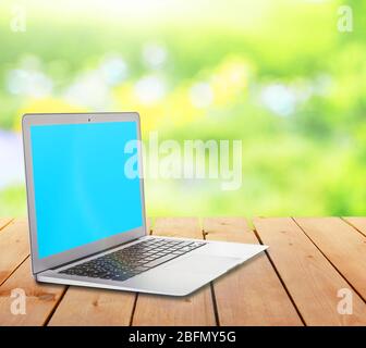 Laptop over wooden table on natural  green blurred background Stock Photo