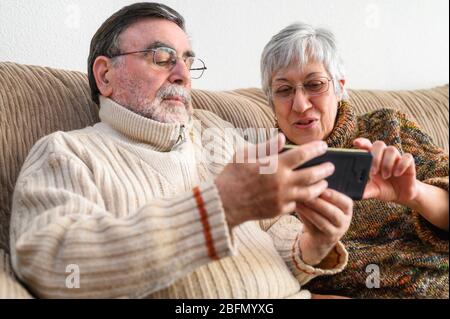 Covid-19 stay home. Happy retired senior couple, doing a family video call with mobile phone. Social distancing, positive expression . Stock Photo
