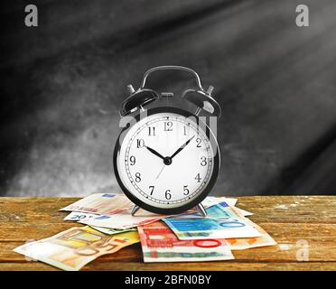 Alarm clock and money on wooden table, grey background Stock Photo