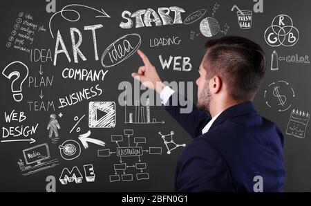 Back view of young man in navy suit pointing on blackboard. Start up concept Stock Photo