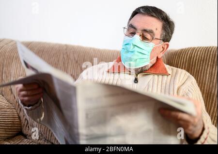 Elderly man reading newspaper during coronavirus epidemic quarantine . Stock Photo
