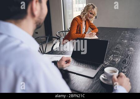 Dark-haired young man sitting beside his coworker Stock Photo