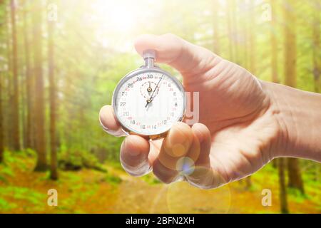 Man holding stopwatch against forest background.Time concept Stock Photo